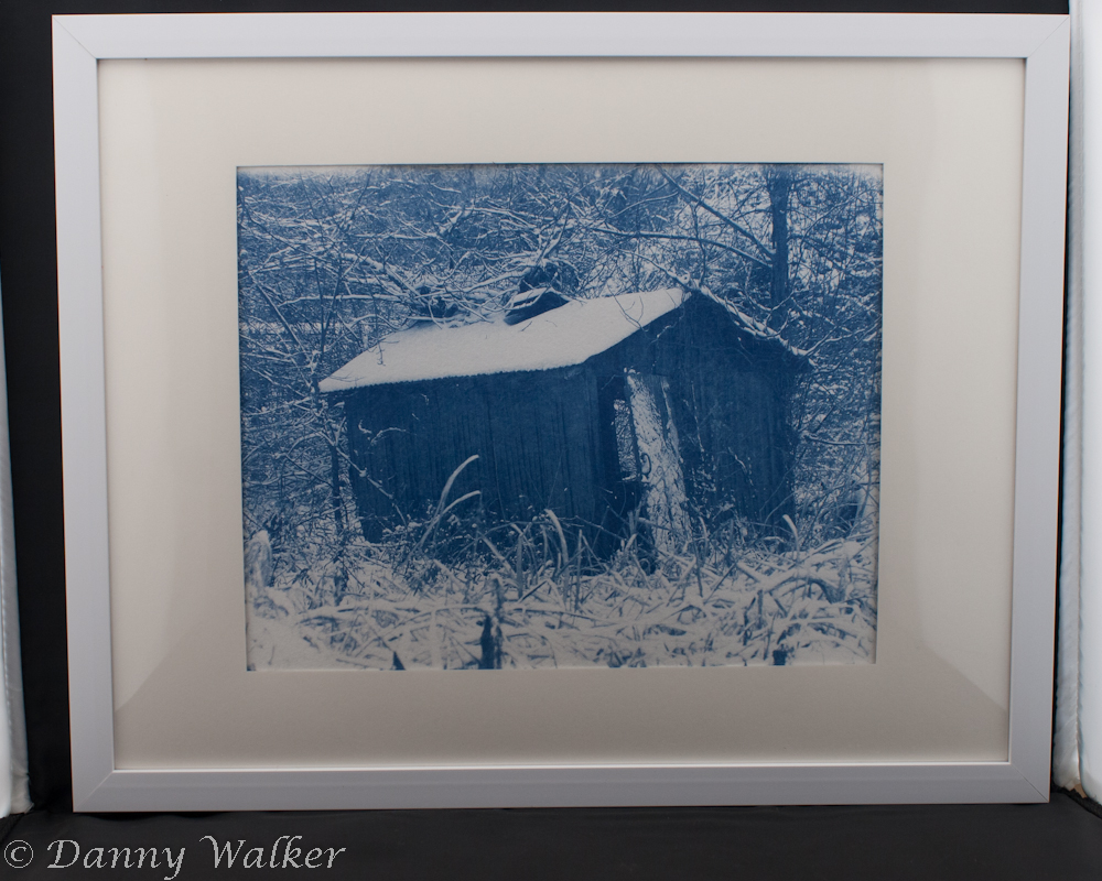 A cyanotype print of a single shack covered in snow.