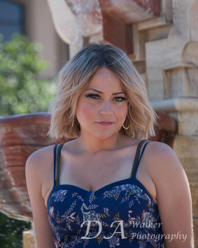Young blond woman with a blue top standing in front of a fountain.